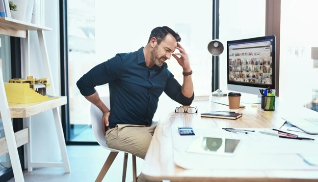 A man suffering from back pain due to poor posture struggles to find relief while working in his Maryland office.