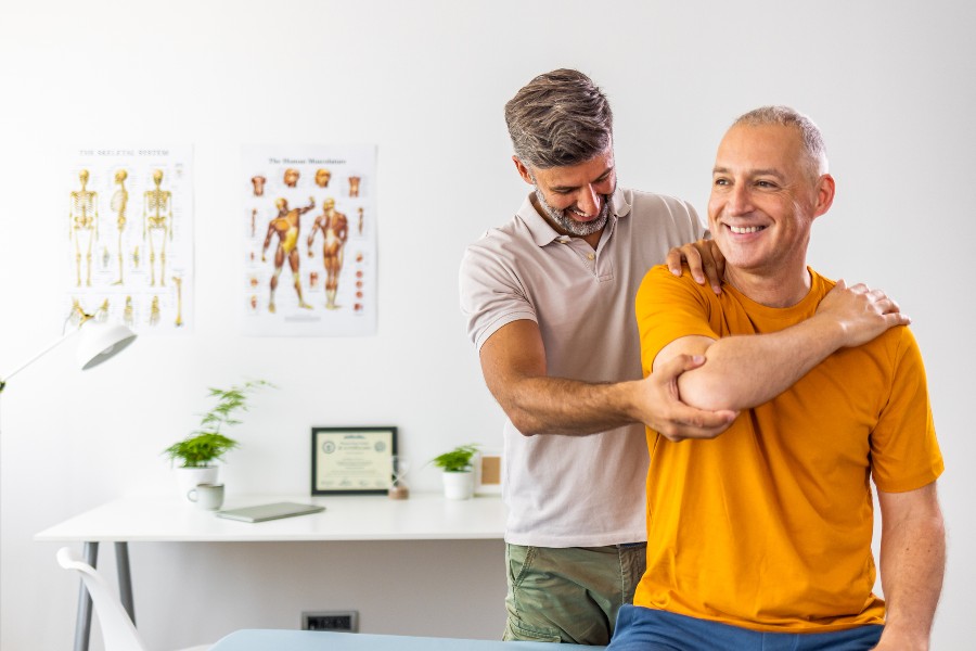 A physio helps a man with his shoulder joint pain with a good stretch