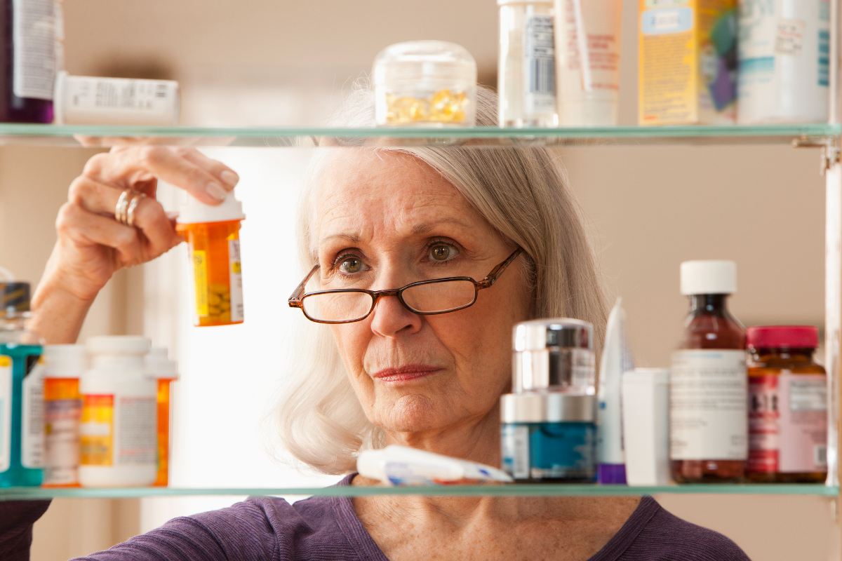 A woman stands before her medicine cabinet examining different pain medications in Greater Maryland.